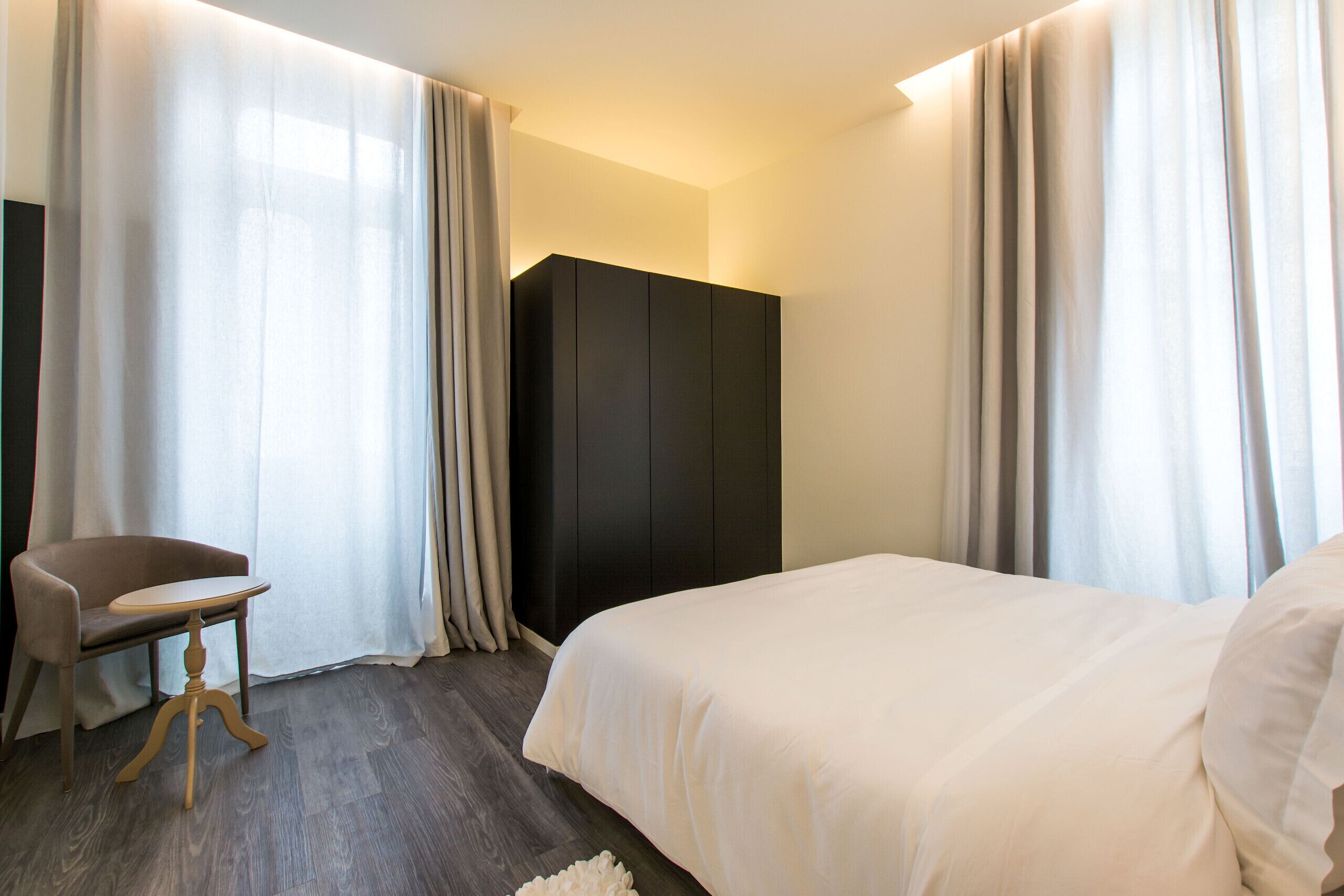 Une chambre d’hôtel avec un lit, une chaise, une armoire et des rideaux.