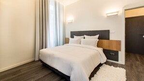 A modern hotel room with a large bed, a wooden headboard, a white rug, and a door with a dark frame. - Letheshome Apartments 307 (Oporto)