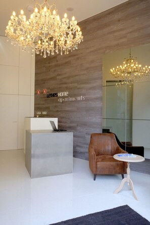 A modern reception area with a chandelier, a reception desk, a leather chair, and a small table. - Letheshome Apartments 309 (Oporto)
