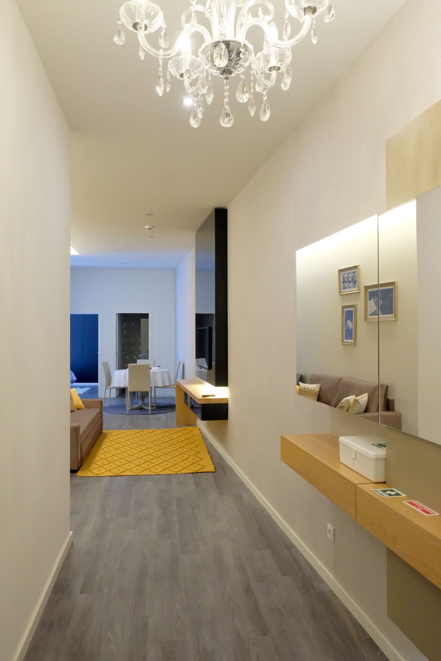 Une chambre d’hôtel moderne, avec un lustre, un coin repas à l’arrière-plan et un grand miroir.