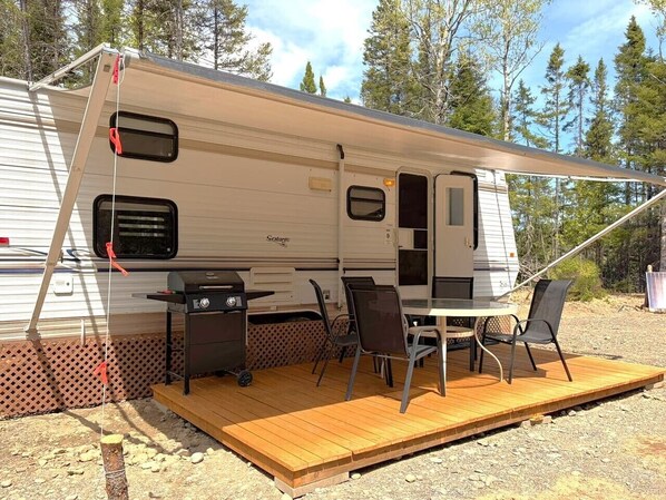 A recreational vehicle with a covered patio area, a grill, and a table with chairs.