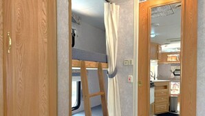 A compact RV interior with a bunk bed, a kitchenette, and a bathroom.