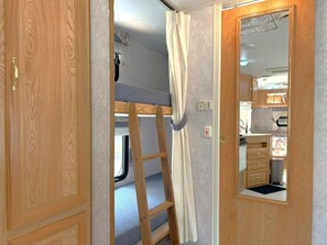 Interior d'una caravana compacta amb un llit superposat, una cuineta i un bany.