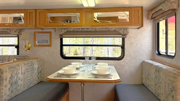 A compact RV interior with a dining area, built-in cabinets, and a window providing a view of the outdoors.