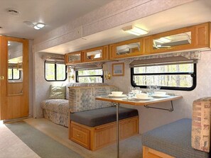A compact RV interior with a kitchenette, seating area, and windows.
