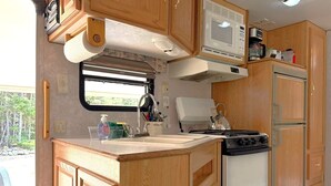 A compact RV kitchen with wooden cabinets, a microwave, a stove, and a refrigerator.