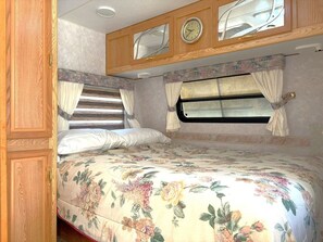 A bedroom with a bed, curtains, a window, and a clock on the wall.