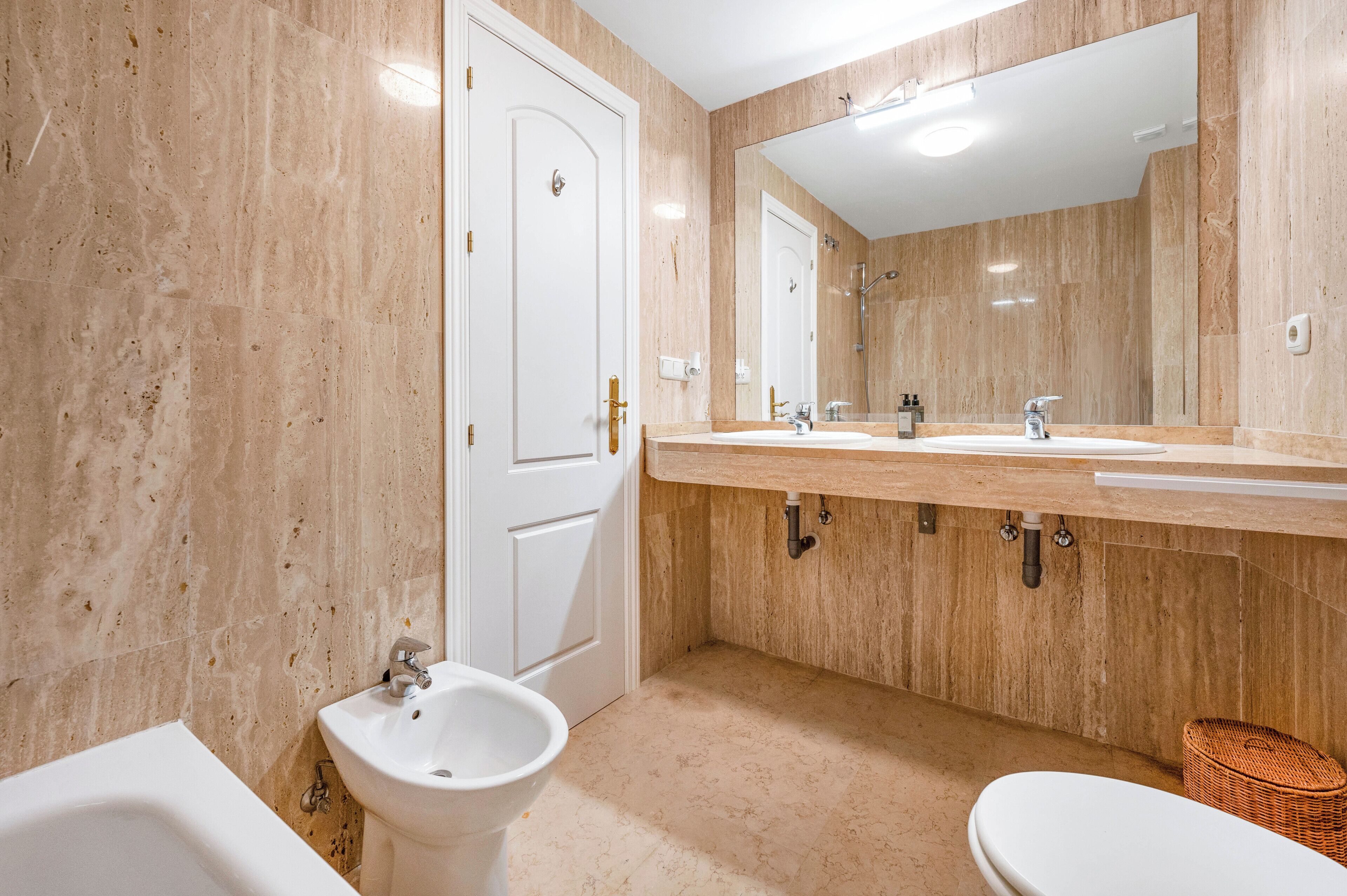 Een badkamer met een wastafel, bidet, toilet en een grote spiegel.