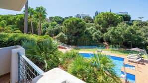 A pool area with a view of a hillside, palm trees, and a building in the background. - LXR Elviria Hills 2-Bedroom Apartment with Heated Pool (Marbella)