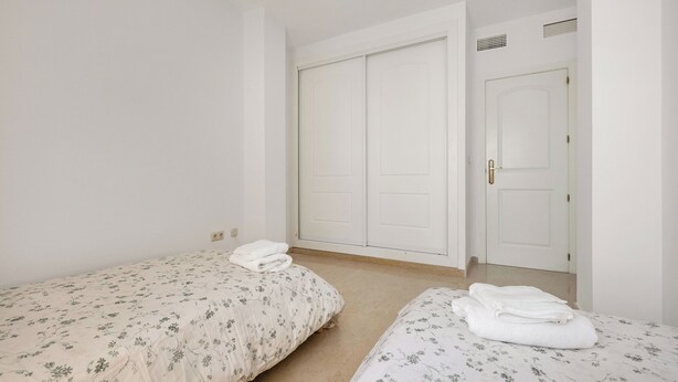 A room with two single beds, a wardrobe, and a door. - LXR Elviria Hills 2-Bedroom Apartment with Heated Pool (Marbella)