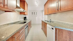 A kitchen with wooden cabinets, granite countertops, a stove, and a dishwasher. - LXR Elviria Hills 2-Bedroom Apartment with Heated Pool (Marbella)