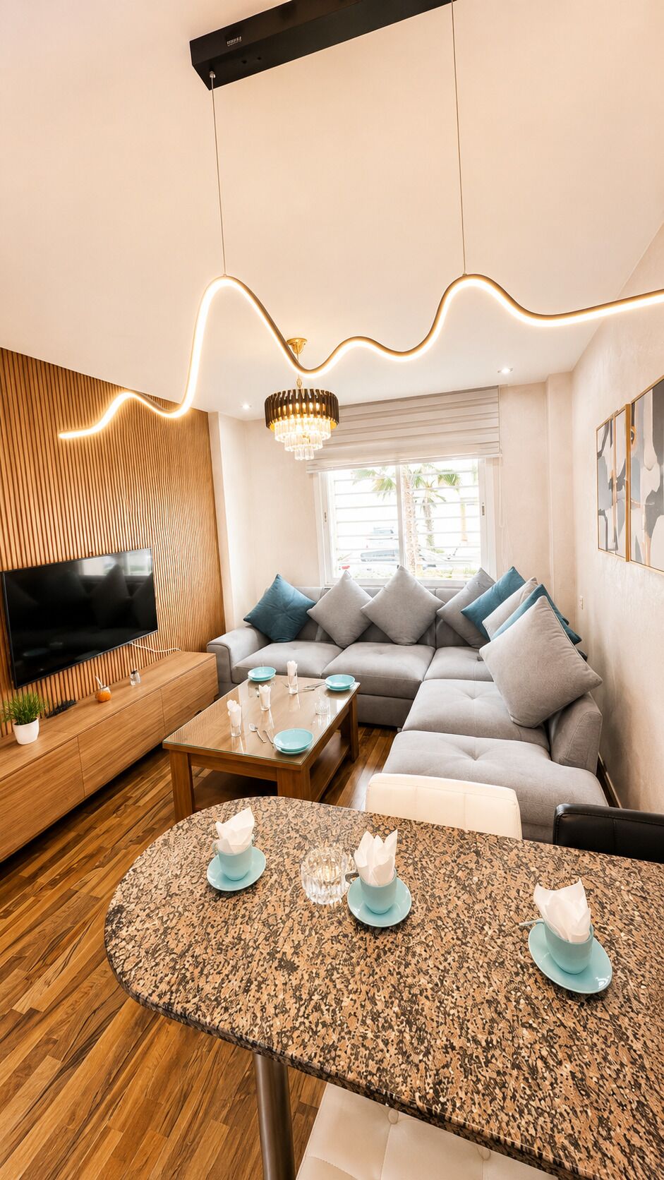 A modern living room with a flat-screen TV, a sofa set, a dining table, and a unique ceiling light fixture.