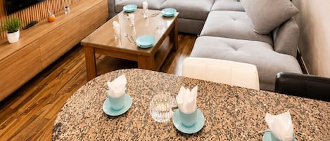 A modern living room with a flat-screen TV, a sofa set, a dining table, and a unique ceiling light fixture.