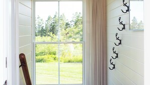A hallway with a wooden floor, a patterned rug, a black doormat, a window with a view of greenery, and a ceiling light fixture. - Modern Guest Suite with Gym & Sauna (Pubnico)