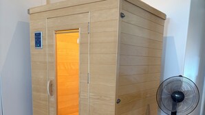 A sauna with a wooden exterior, a glass door, and a fan nearby. - Modern Guest Suite with Gym & Sauna (Pubnico)