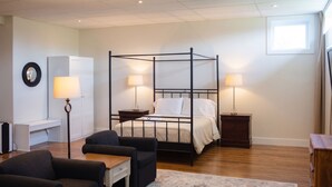 A four-poster bed with two bedside tables, a desk, two chairs, a patterned rug, and a small window. - Modern Guest Suite with Gym & Sauna (Pubnico)