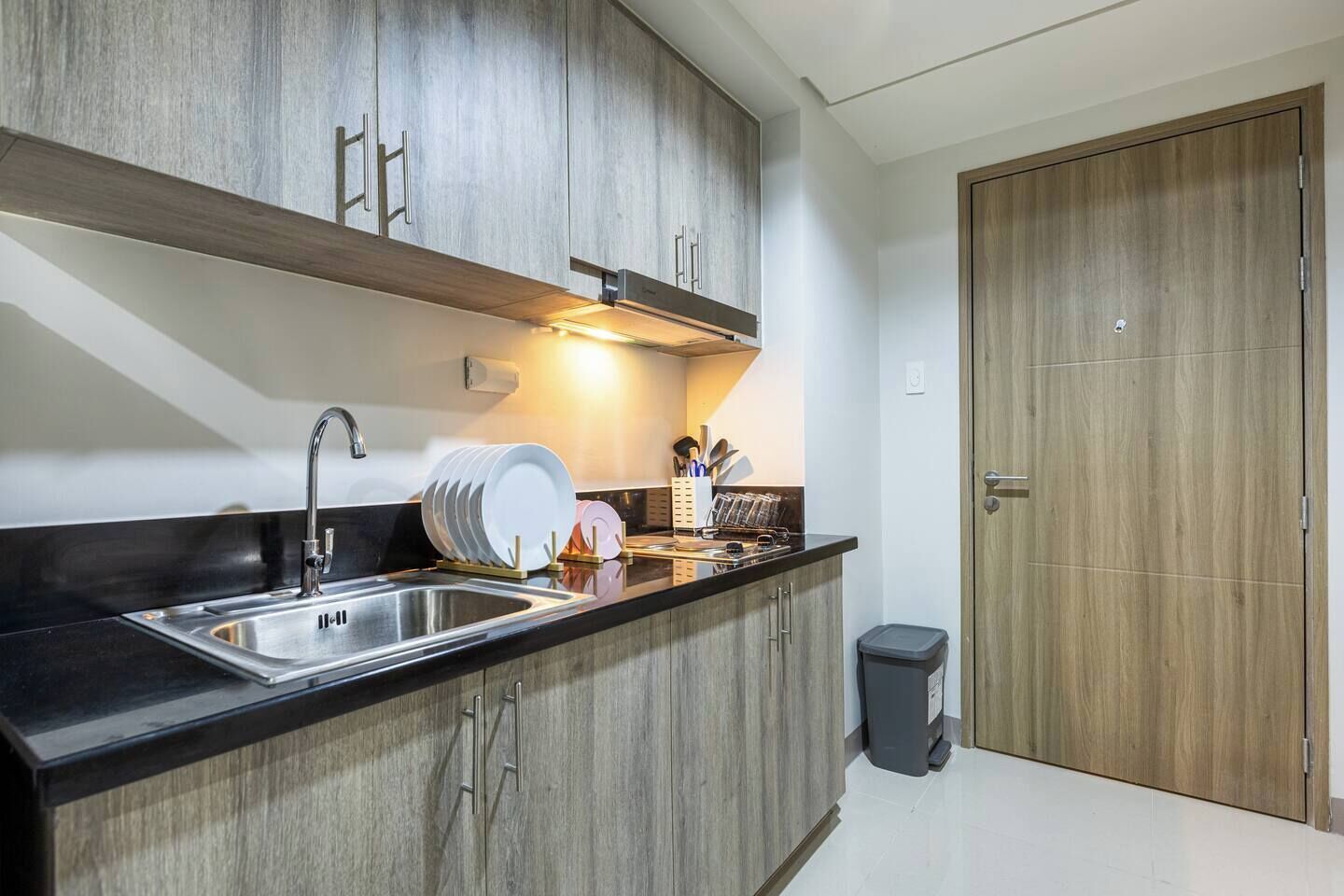A modern kitchen with a black countertop, stainless steel sink, wooden cabinets, and a built-in oven.