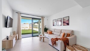 Una sala de estar moderna con un sofá, una mesa de centro, televisor y puertas de vidrio corredizas que dan a un balcón.