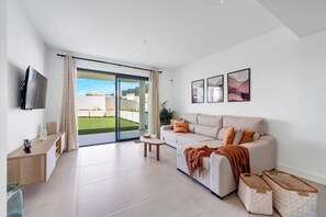 A modern living room with a sofa, coffee table, TV, and sliding glass doors leading to a balcony. - LXR Higueron Privé 2-Bedroom Stays (Fuengirola)
