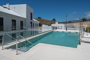A swimming pool with a glass barrier, a white building, and a stone wall in the background. - LXR Higueron Privé 2-Bedroom Stays (Fuengirola)