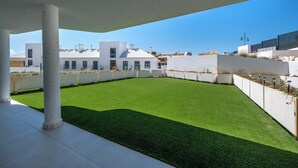 Una terraza con césped artificial, columnas blancas y edificios modernos al fondo.
