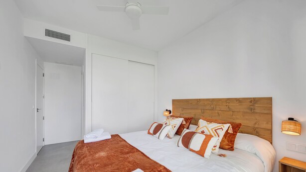 Una cama bien hecha con cabecera de madera, ropa de cama blanca y almohadas decorativas.