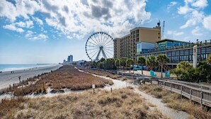 Vista à beira-mar com uma roda gigante, calçadão e um hotel com varandas com vista para a praia.