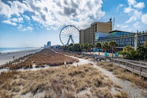 Blick auf einen Strand mit Riesenrad, Promenadenweg und einem Hotel mit Balkonen mit Meerblick.