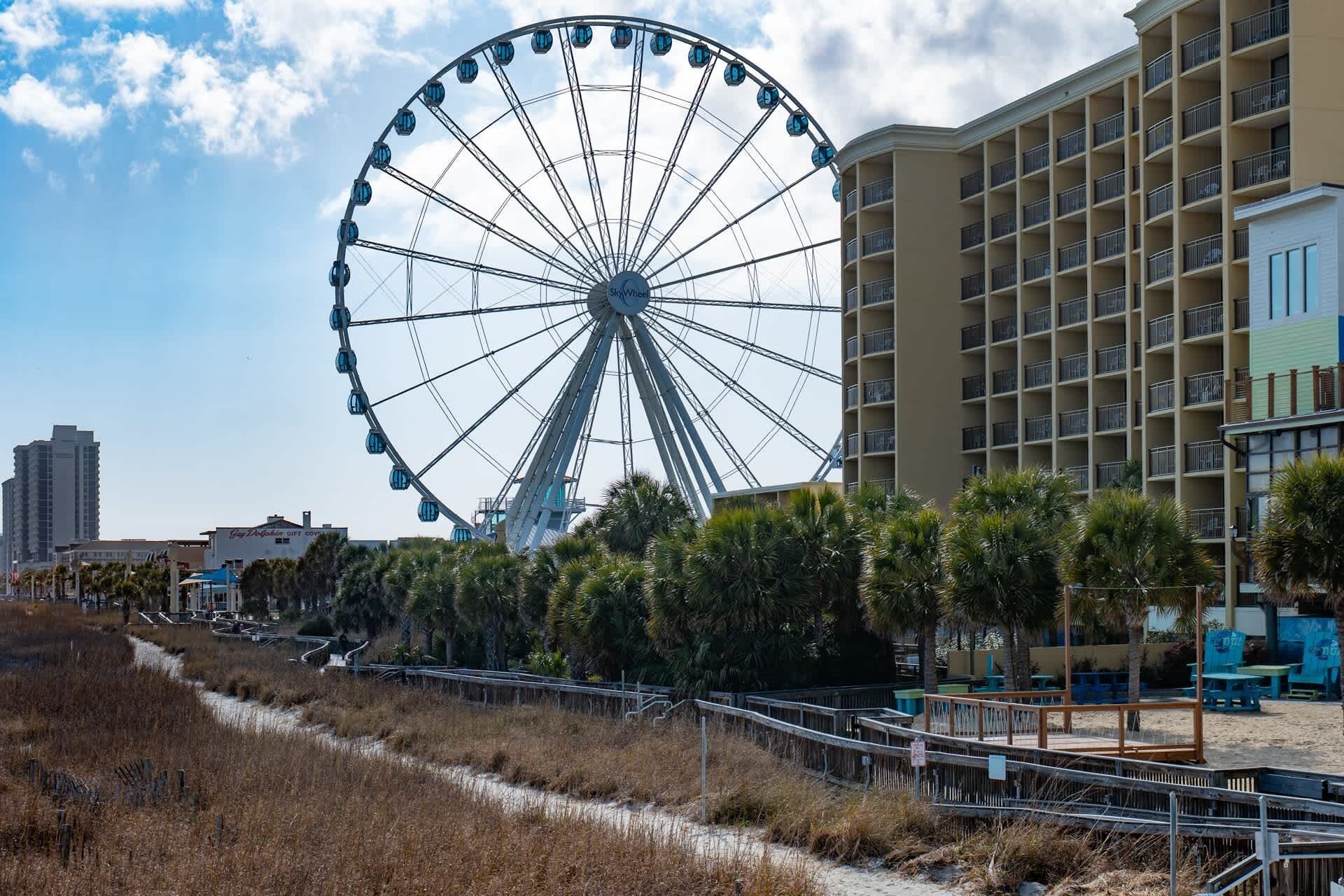 Une grande roue, une promenade en bord de mer et un hôtel à plusieurs étages doté de balcons.