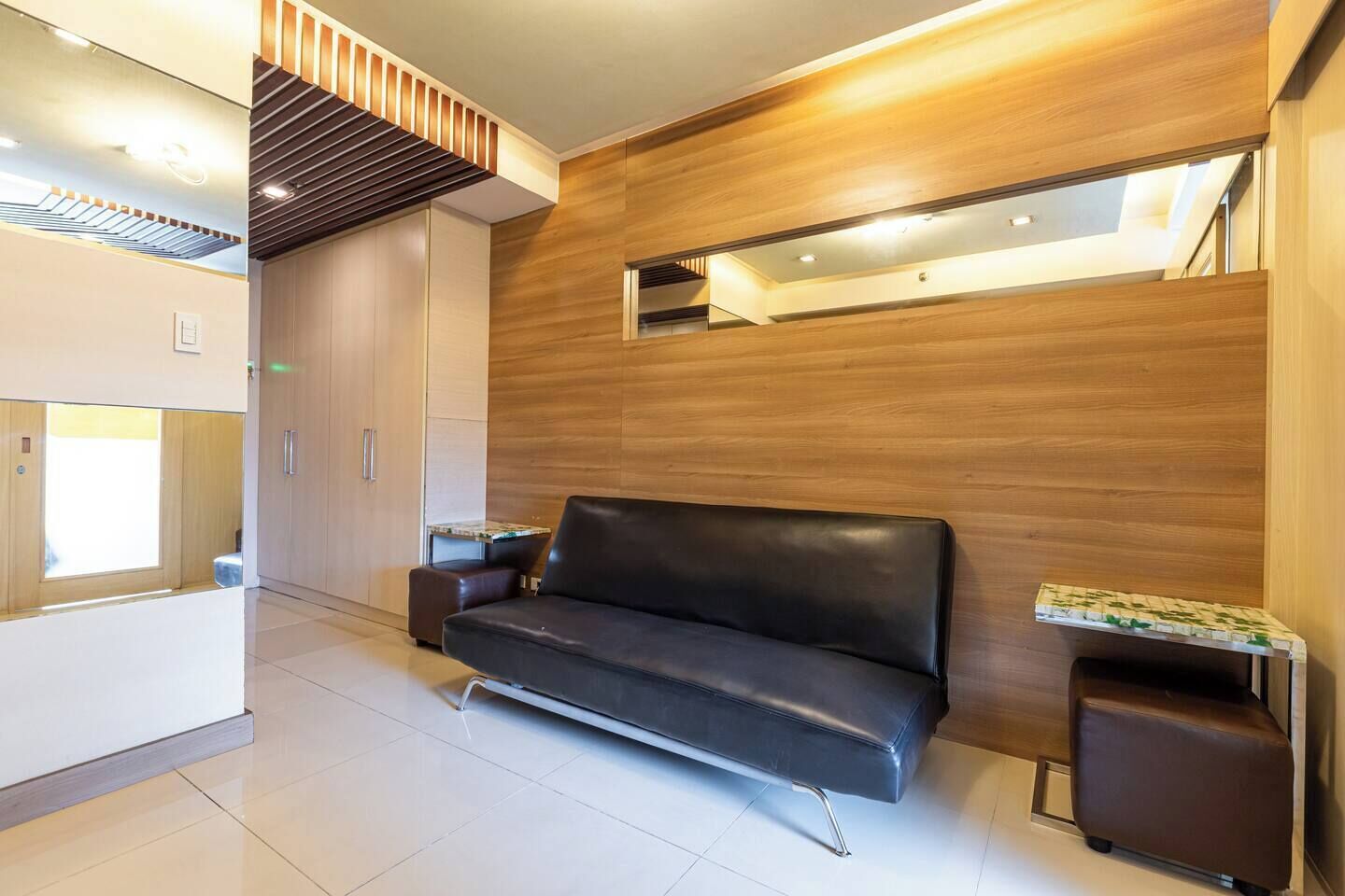 Habitació d'hotel moderna amb un sofà de pell negra, parets de panells de fusta i una finestra petita.