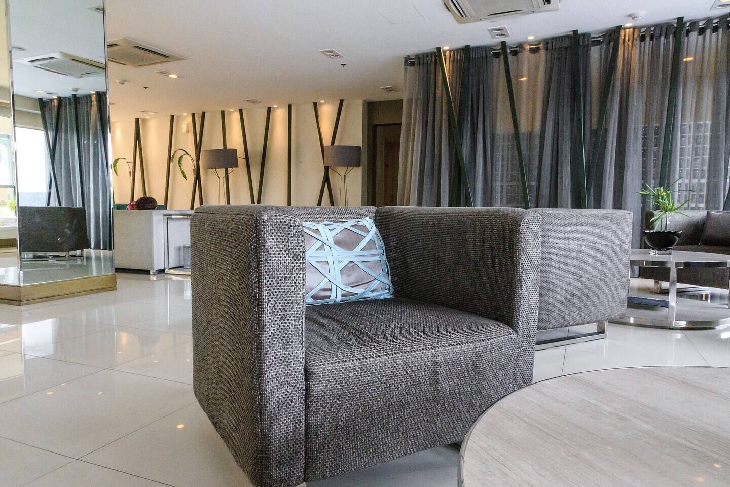 A modern hotel lobby with a seating area, a reception desk, and a large window with curtains.