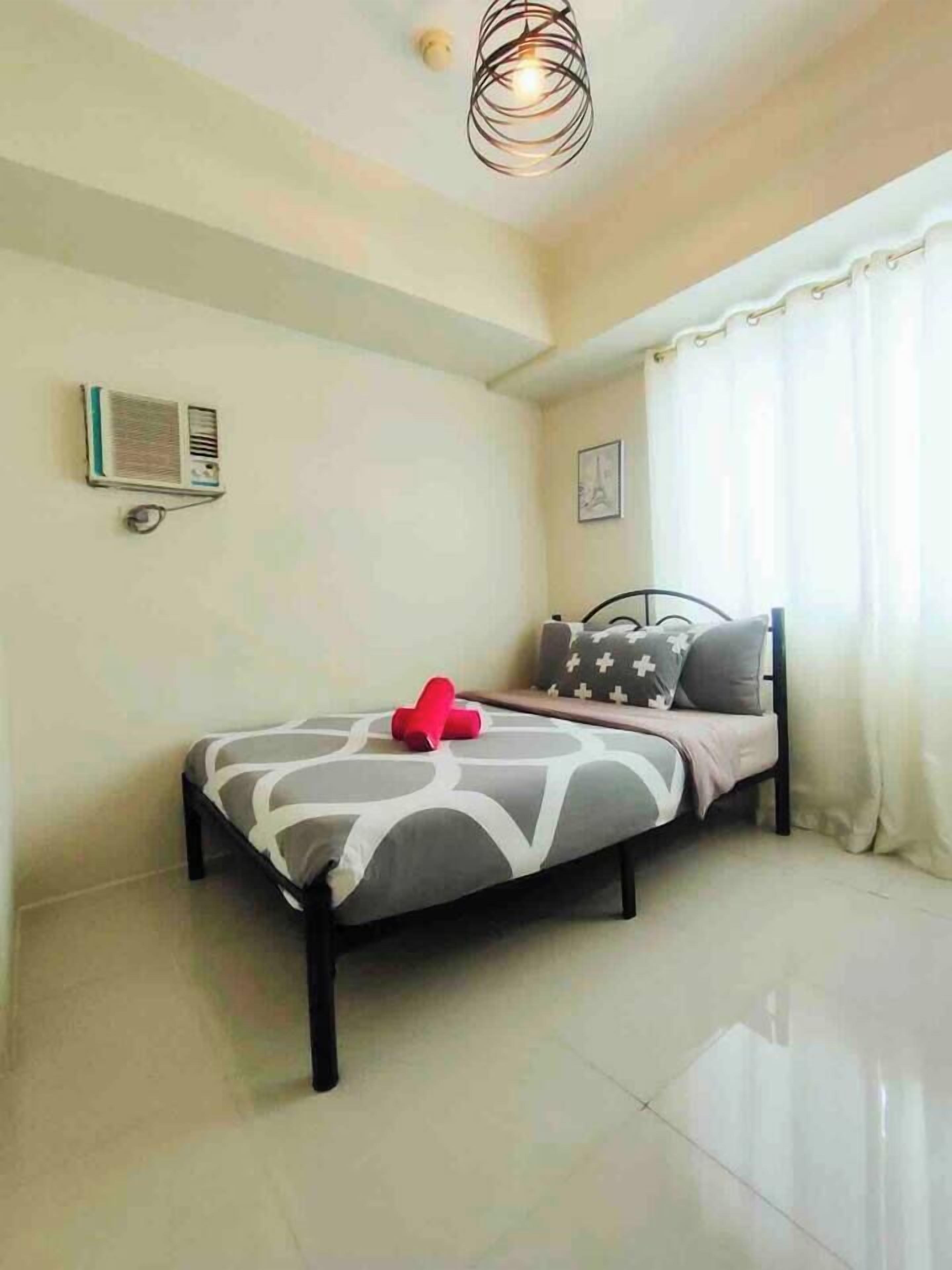 A bedroom with a bed, a ceiling light fixture, an air conditioning unit, and a window with curtains.