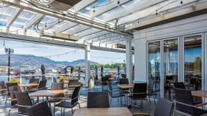 Un café al aire libre con mesas y sillas, vista al puerto y una zona acristalada con vistas panorámicas de la ciudad.
