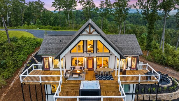 Une maison à deux étages dotée d’une terrasse, de grandes fenêtres et offrant une vue sur la forêt environnante.