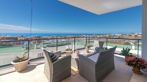 A balcony with wicker furniture, potted plants, and a view of the city and sea. - LXR Hollywood Hills 2-Bedroom: Stunning Views (Mijas)