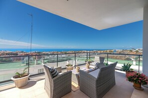 Ein Balkon mit Korbmöbeln, Topfpflanzen und Blick auf Stadt und Meer.