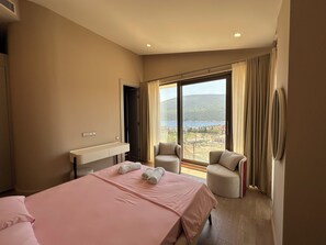 A hotel room with a bed, two chairs, a vanity, and a large window with a view.