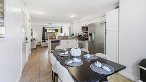 A modern kitchen with white cabinets, stainless steel appliances, and a dining area set with placemats and napkins. - Black & White Oasis+ heated pool, close to Siesta (Sarasota)
