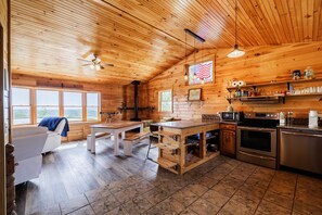 A wooden cabin interior with a kitchen, dining area, and a large window. - Bella Vista  50 Acres, Pond, Hot Tub & Game Room (Dalton)