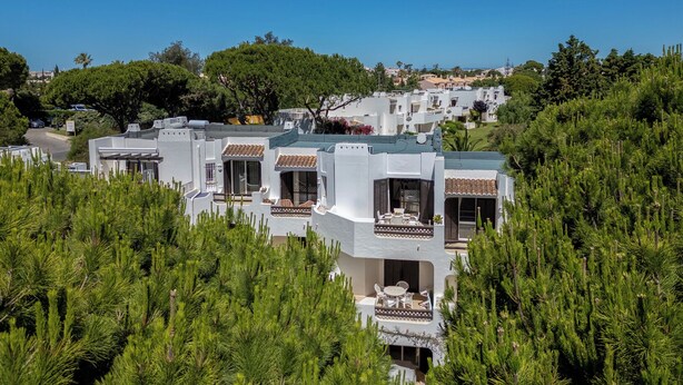 A modern resort with multiple white buildings, outdoor seating areas, and lush greenery.