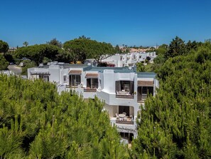 Et moderne resort med flere hvide bygninger, udendørs siddeområder og frodigt grønt område.