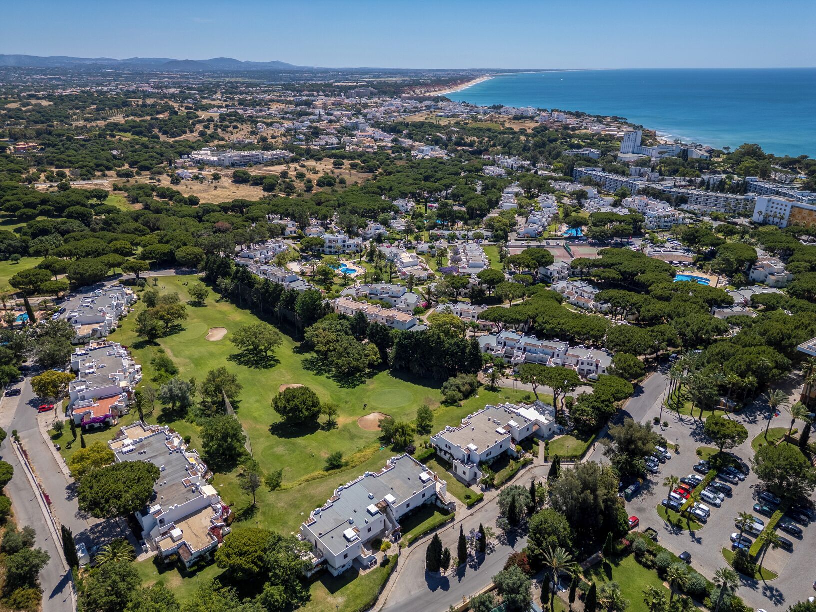 An aerial view of a coastal residential area with houses, a golf course, and a beach.