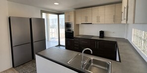 A modern kitchen with stainless steel appliances, dark cabinetry, and a large window.
