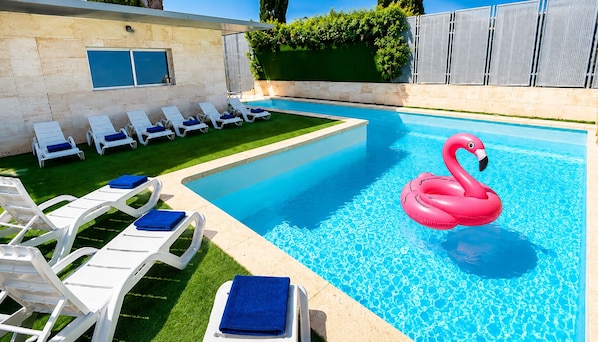 A swimming pool with white lounge chairs and a pink flamingo float.