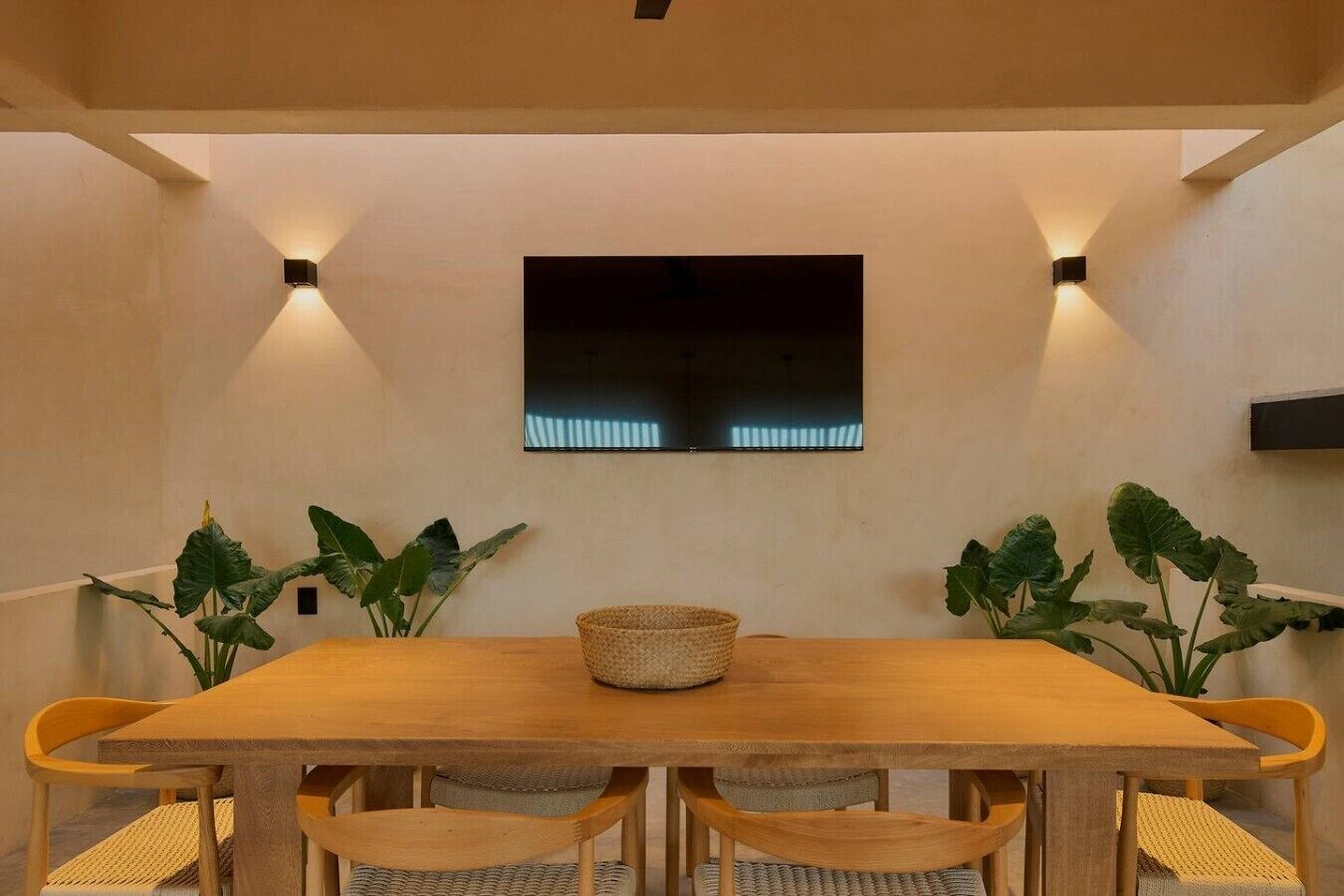 Un coin repas comprenant une table en bois, quatre chaises, deux lampes fixées au mur et un téléviseur à écran plat.