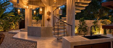 A modern outdoor area with a concrete staircase, a seating area, and hanging light fixtures.