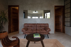 Un salon avec un canapé en cuir marron, une table basse ronde, une table d’appoint en bois et une plante en pot.
