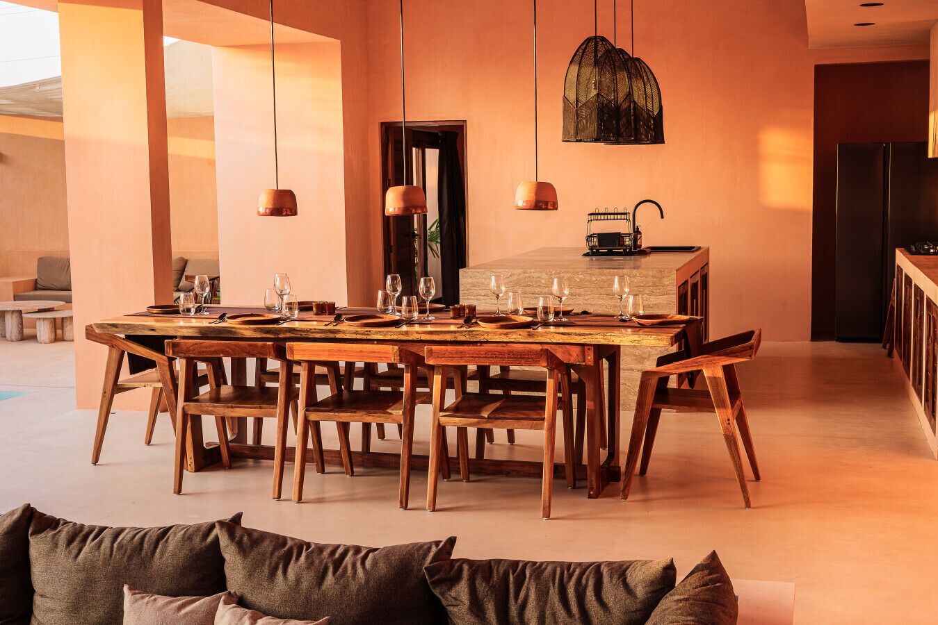 Un comedor con una mesa y sillas de madera, luces colgantes y una cocina con refrigerador.