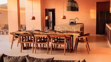 Un comedor con una mesa y sillas de madera, luces colgantes y una cocina con refrigerador.