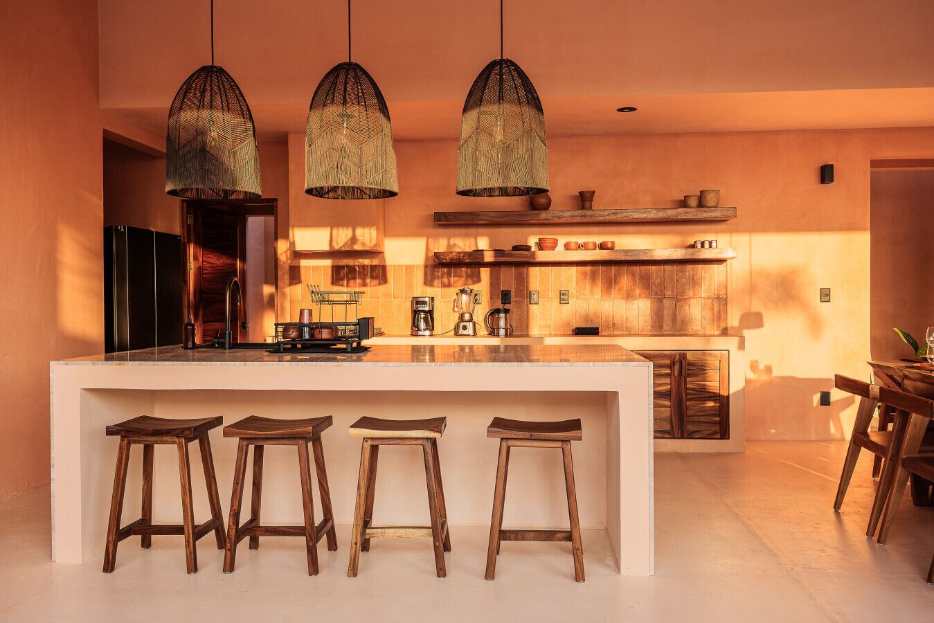 Una cocina moderna con una isla central, taburetes de madera, lámparas colgantes y una zona de bar de madera.